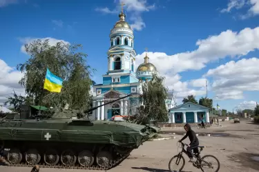 Un niño monta en bicicleta cerca de un tanque blindado con una bandera ucraniana en la ciudad de Izium, recientemente liberada por las Fuerzas Armadas