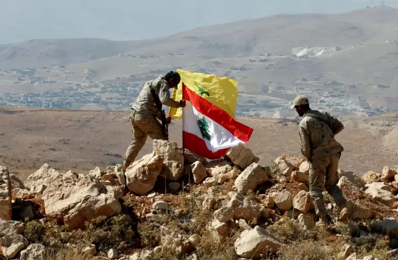 Miembros de Hezbolá izando la bandera de la organización junto a la nacional de Líbano en una colina, reflejando la compleja dinámica paraestatal